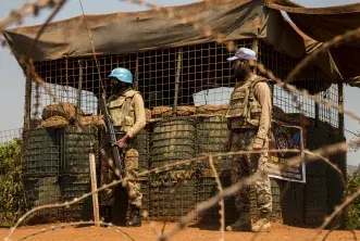 Two UN Peacekeepers stand behind barbed wire 